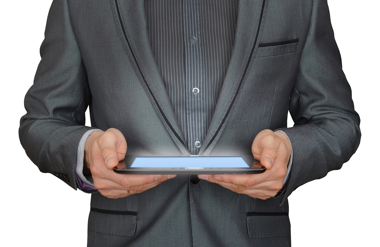 A man in a grey suit holding a glowing tablet, face out of frame