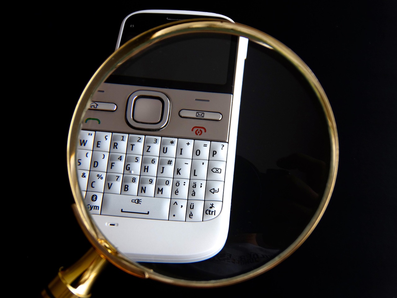 A magnifying glass lying over a phone keyboard on a black background