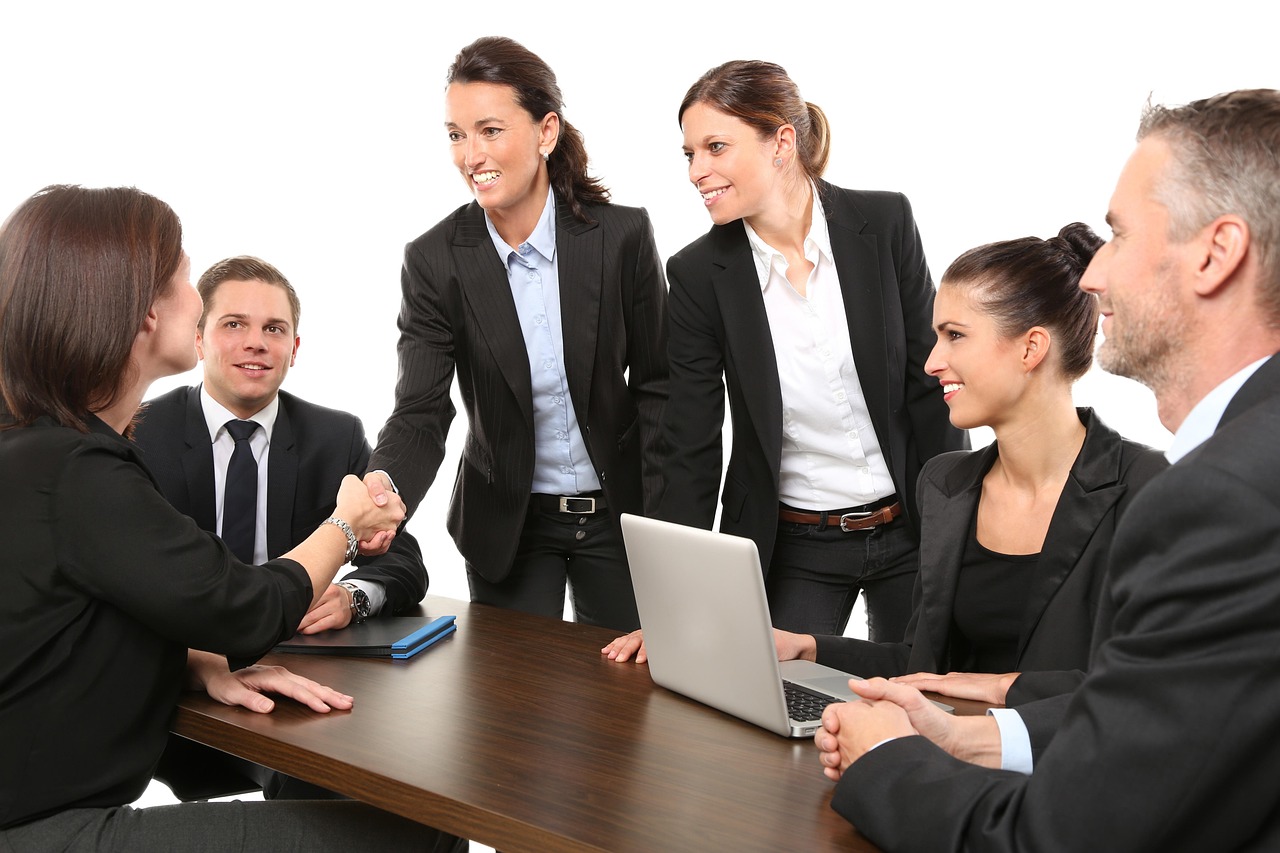 Five business people at a conference table, one handshake and a closed laptop